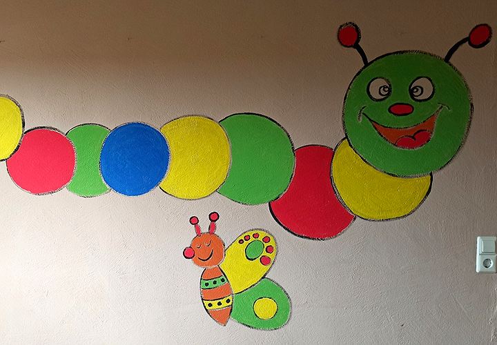 Eine große bunte Raupe mit lachendem Gesicht, an die Wand des Spielzimmers gemalt, darunter eine Biene